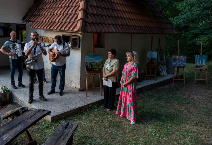 Ispred kuce ljudi koji govore, do njih muzicar koji svira na gitari