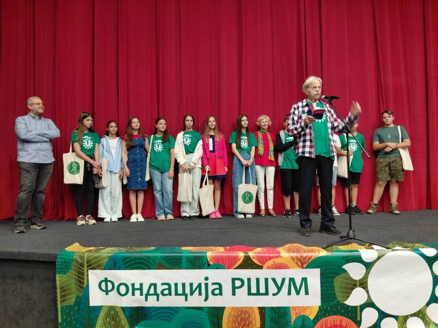 deca na sceni ispred njih stoji odrastao covek i recituje