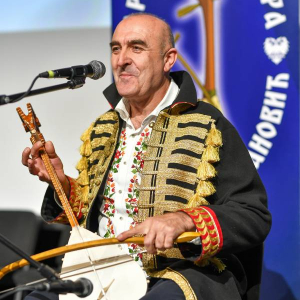 Гуслар са инструментом у наручју. Испред њега је микрофон. 
