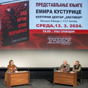 Сцена на којој се виде три мушкарца која седе и разговарају. Пред њима су столови са књигама. Иза њих је пано са најавом промоције.