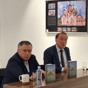 Двојица мушкараца гледају ка објективу. Испред њих су књиге на столу