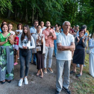 Ljudi stoje i slusaju, a u poyadini je suma