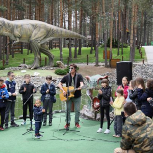 muskarac sa gitarom peva u mikrofon okružen decom