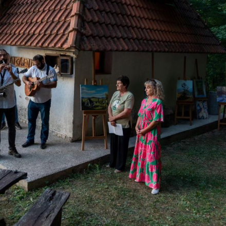 Ispred kuce ljudi koji govore, do njih muzicar koji svira na gitari